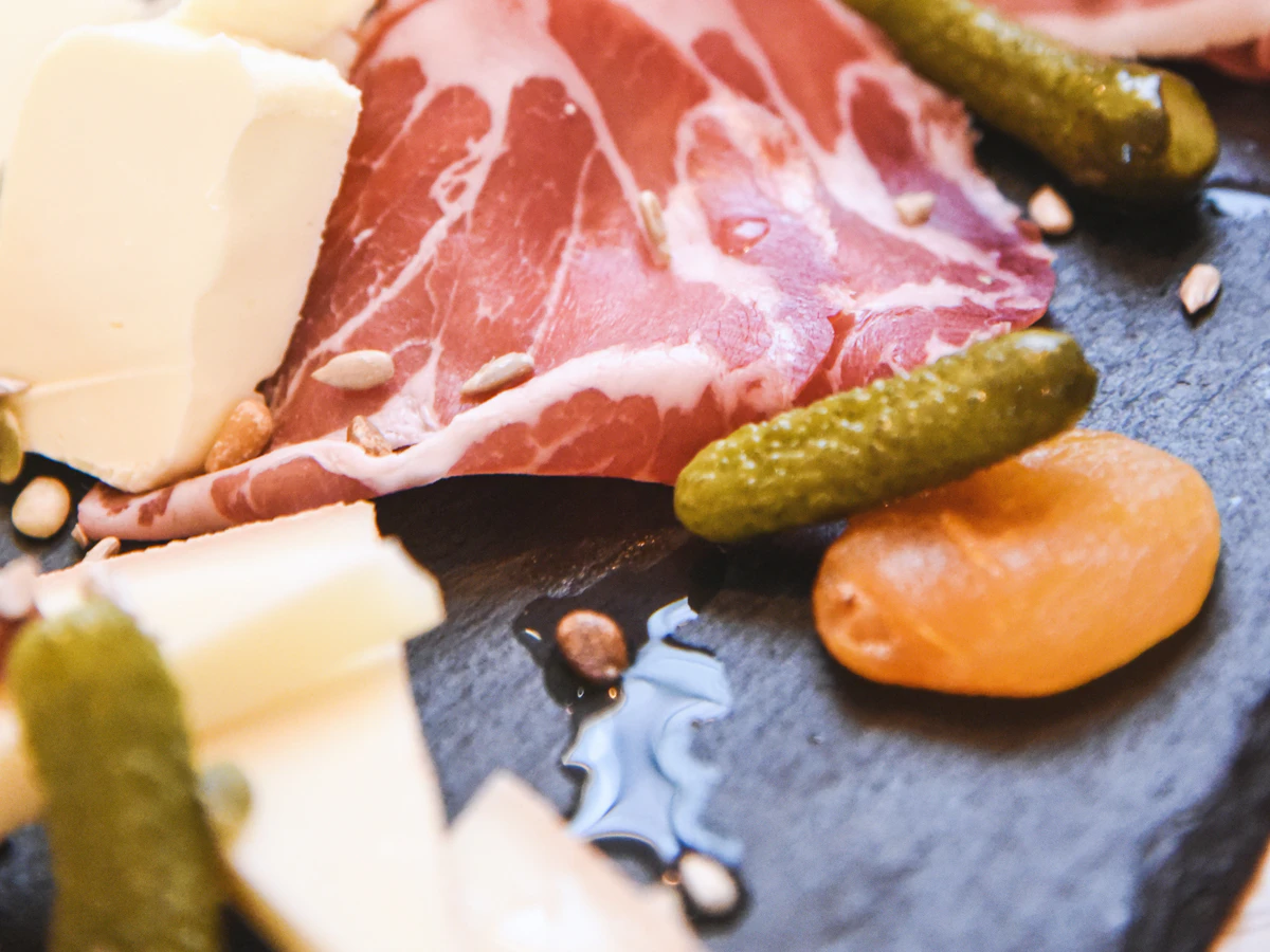 Thin slices of cured meat with cheese, cornichons and dried apricot on slate.