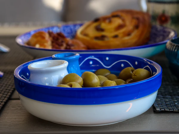 Green olives and a small jug of olive oil in a blue and white ceramic dish.
